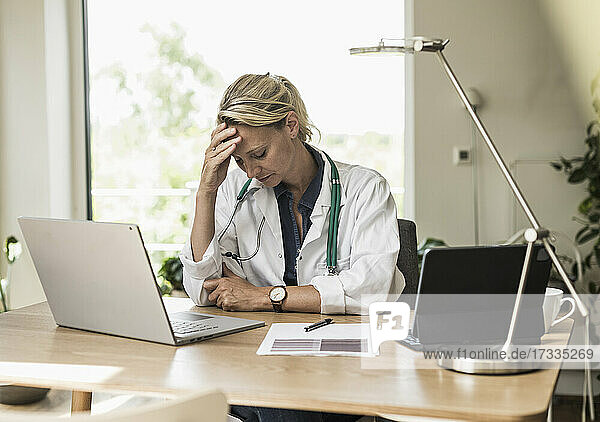 Arzt mit Kopf in den Händen sitzt am Schreibtisch im Büro