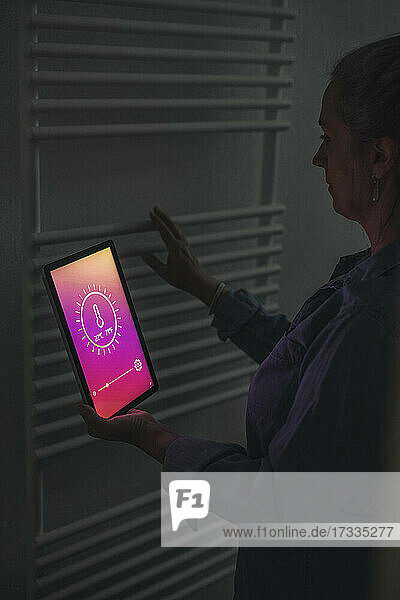 Frau prüft zu Hause stehend die Raumtemperatur mit Hilfe eines digitalen Tablets