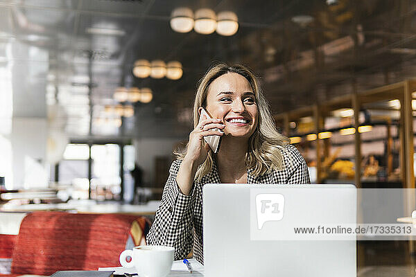 Lächelnde weibliche Fachkraft  die mit einem Mobiltelefon spricht  während sie im Café wegschaut