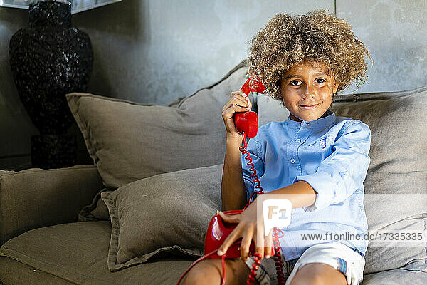 Junge mit Spielzeugtelefon  der zu Hause auf dem Sofa sitzt