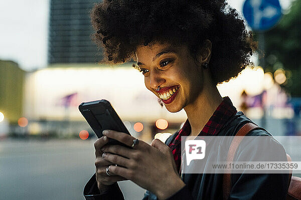 Lächelnde Frau mit Smartphone in der Abenddämmerung