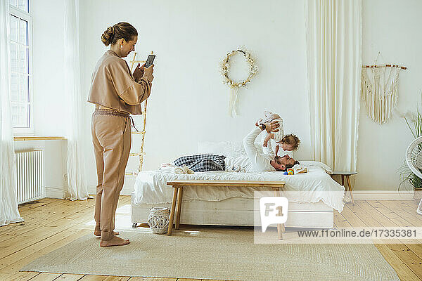 Frau fotografiert Mann beim Spielen mit Tochter auf dem Bett zu Hause