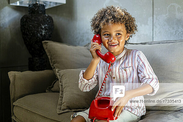 Afro Junge lächelnd beim Spielen mit Spielzeug Telefon auf dem Sofa