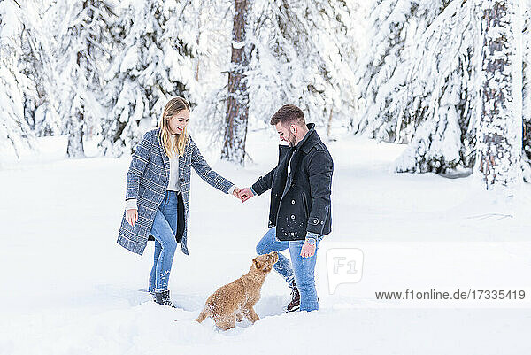 Couple holding hands while looking at dog in snow during vacation