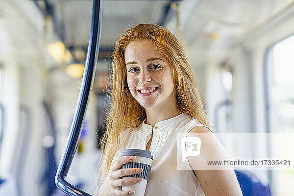 Beautiful businesswoman smiling while holding disposable coffee cup in train