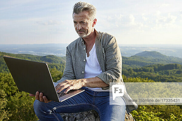 Man using laptop while sitting on mountain