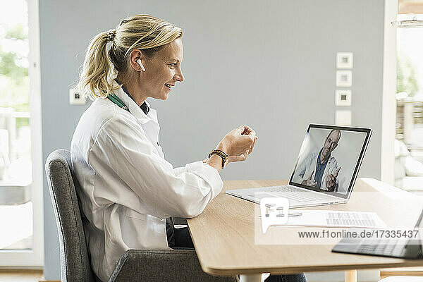 Eine Ärztin diskutiert mit einem männlichen Kollegen per Videoanruf am Laptop im Büro