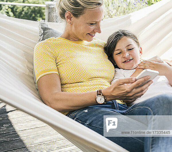 Smiling woman using mobile phone while resting with girl on hammock