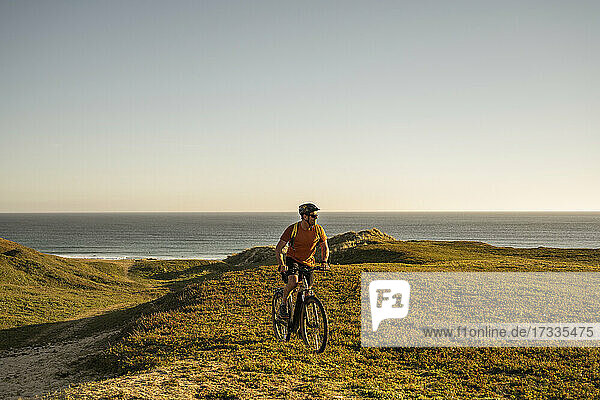 Male sportsperson cycling on green landscape at sunset