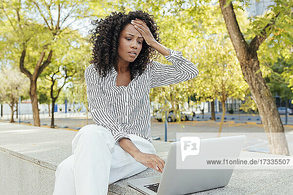 Besorgte Geschäftsfrau sitzt mit Laptop im Büropark