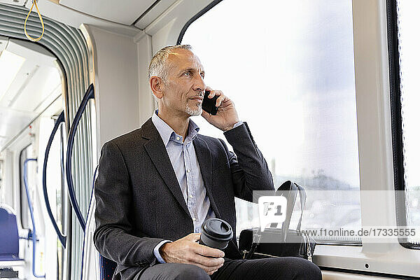 Geschäftsmann  der in der Straßenbahn sitzt und mit seinem Smartphone telefoniert