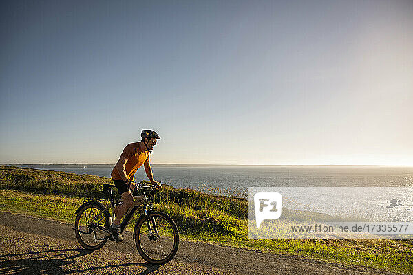 Cheerful mature male athlete riding electric bicycle by sea