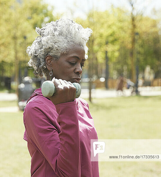 Aktive ältere Frau,  die im öffentlichen Park mit einer Hantel trainiert