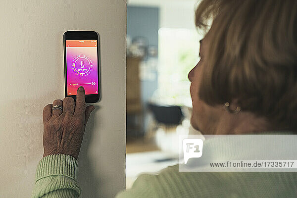 Ältere Frau steuert die Raumtemperatur über ein Hausautomatisierungsgerät