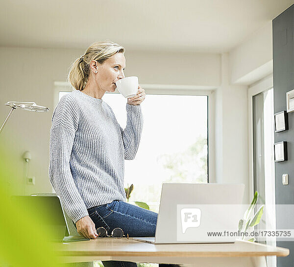 Female freelancer drinking coffee while sitting by laptop on desk