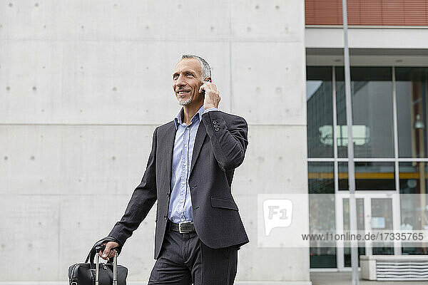 Businessman talking on smart phone while standing outside office building