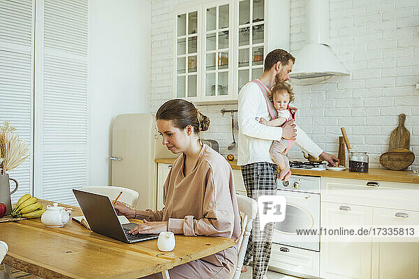 Geschäftsfrau mit Laptop und Mann mit Tochter bei der Zubereitung von Speisen in der Küche