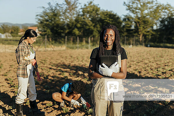 Smiling female farmer standing with digital tablet at organic farm during sunny day