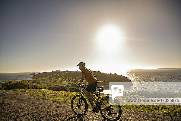 Male sportsperson riding electric mountain bike on road by sea