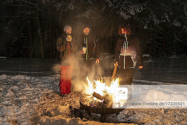 Die Familie steht im Winter nachts am Lagerfeuer zusammen