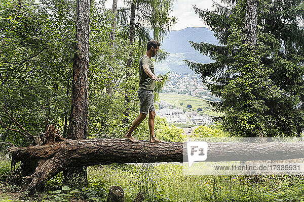 Man walking with arms outstretched on fallen tree in forest