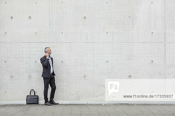 Businessman talking on smart phone while standing near wall