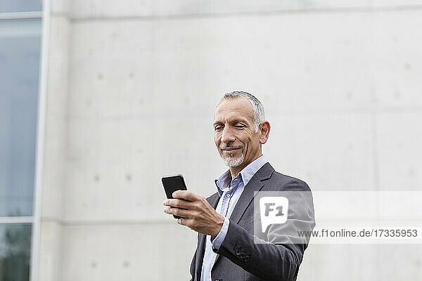 Männlicher Geschäftsmann  der in der Nähe eines Bürogebäudes ein Smartphone benutzt