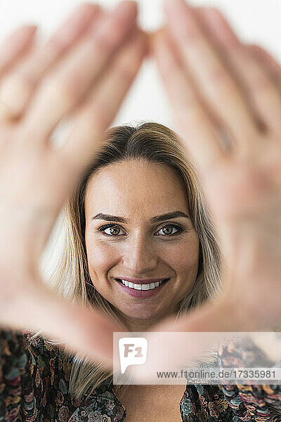 Lächelnde Frau schaut durch den Fingerrahmen