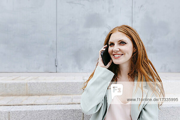 Smiling female professional talking on smart phone in front of wall