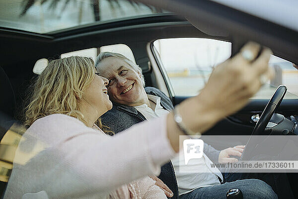 Glückliches reifes Paar  das sich gegenseitig ansieht  während es ein Selfie im Auto sitzt