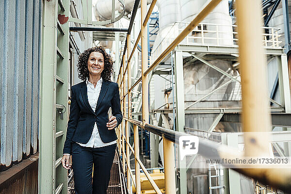 Smiling businesswoman holding mobile phone while walking in industry