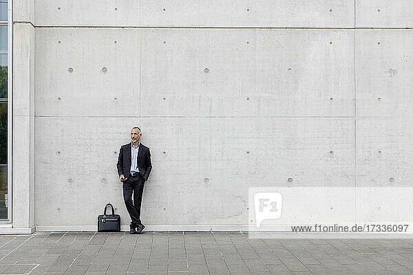 Businessman with hand in pocket standing in front of white wall