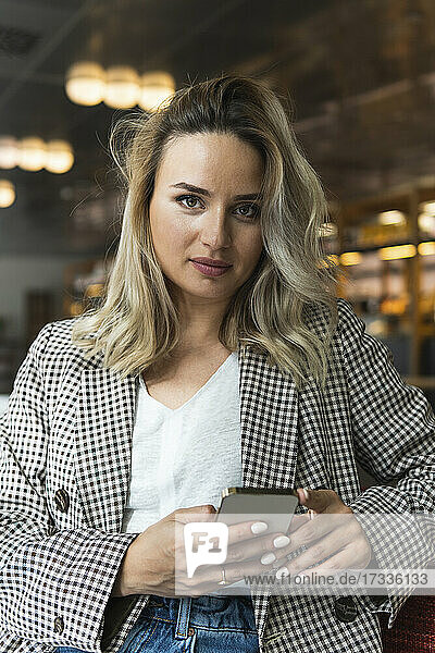 Beautiful businesswoman holding smart phone while sitting at cafe