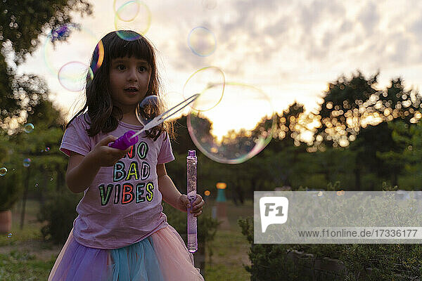 Girl looking with wand looking at soap bubbles while playing during sunset
