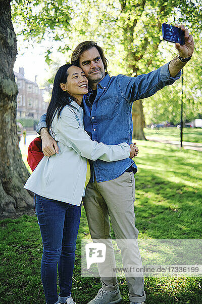 Pregnant couple taking selfie through smart phone in public park