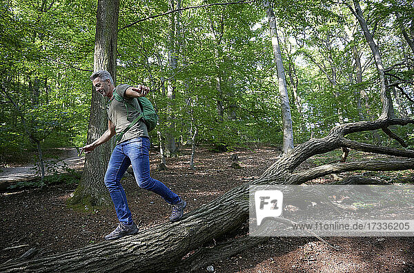 Carefree man with arms outstretched walking on fallen tree in forest