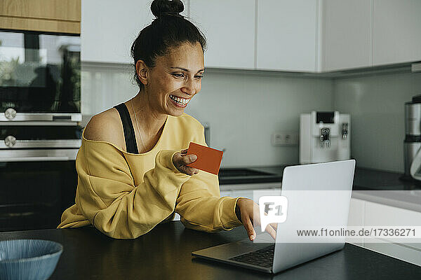 Lächelnde Frau beim Online-Einkauf mit Kreditkarte an der Kücheninsel