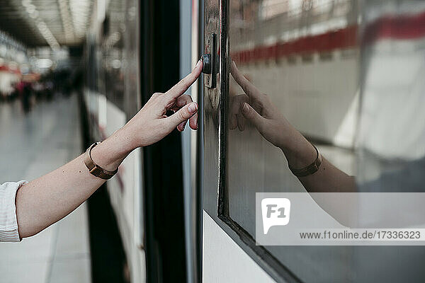 Junge Frau drückt am Bahnhof auf einen Knopf im Zug