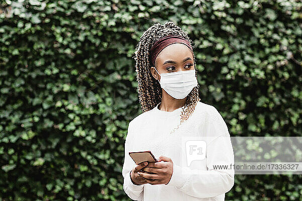 Young woman wearing protective face mask holding smart phone