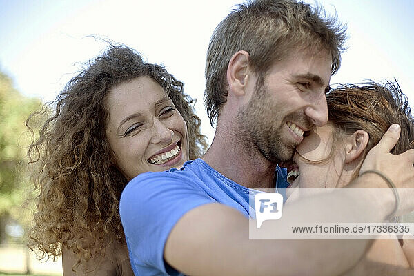 Glückliche lockig behaarte Frau schaut auf ein sich umarmendes Paar im Park