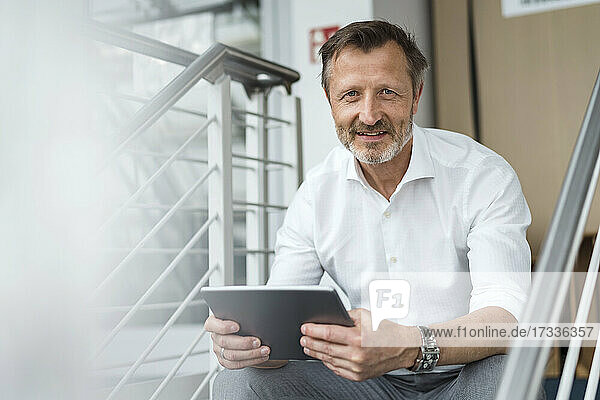 Männlicher Fachmann  der ein digitales Tablet hält  während er im Büro sitzt