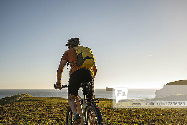 Male athlete with backpack riding mountain bike towards sea