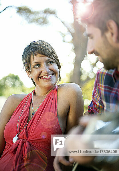 Smiling woman looking at boyfriend playing guitar