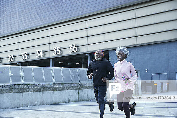 Lächelnde Frau joggt mit Mann vor einem Gebäude