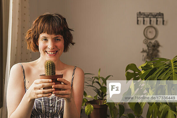 Happy woman with brown hair holding cactus plant at home