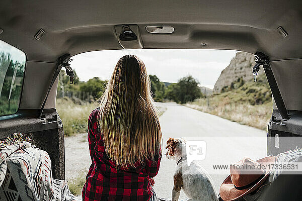 Blonde Frau mit Jack Russell Terrier sitzt im Kofferraum eines Autos