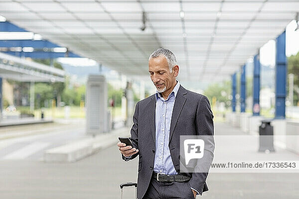 Männlicher Berufstätiger mit Smartphone am Bahnhof
