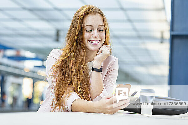 Lächelnde Geschäftsfrau  die ein Mobiltelefon benutzt  während sie sich auf eine Stützmauer stützt