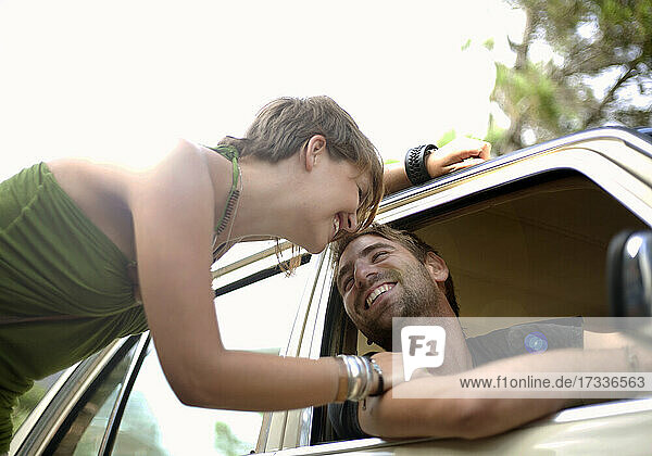 Lächelnde junge Frau lehnt sich im Auto an ihren Freund