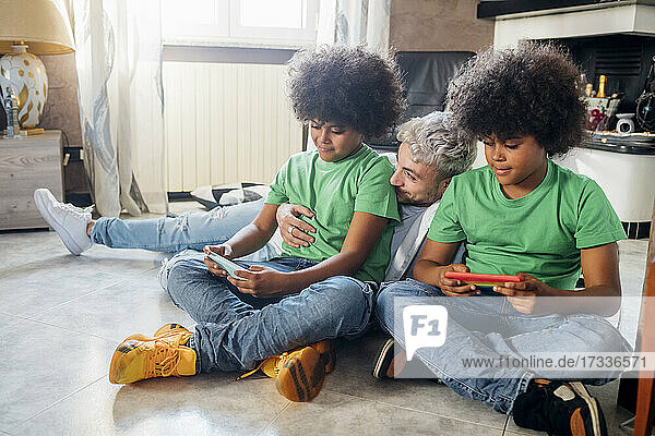 Young man with twin brothers using smart phone while sitting at home